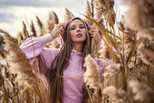 Beauty Girl Outdoors enjoying nature. Beautiful Teenage Model girl wearing a warm pink hoodie on the Autumn Field, Sun Light. Glow Sun. Free Happy Woman. Toned in warm colors