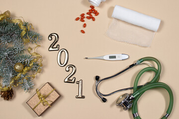 New Year's card on medical subjects: figures 2021, phonendoscope, tablets, thermometer and bandage with spruce branch on a beige background. New Year 2021 medicine.