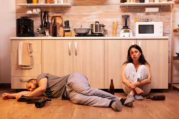 Alcoholic man lying on the floor near beaten wife surrounded by empty bottles. Drunk aggressive...
