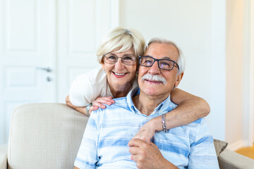 Portrait loving older wife hugging husband sitting on cozy couch. Happy senior mature couple smilling and looking at camera, posing for family photo at home. Elderly couple feeling happy
