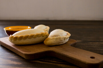 Traditional baked Argentine empanadas savory pastries with meat beef stuffing or vegetables against wooden background and spicy sauce. Latin American fried food