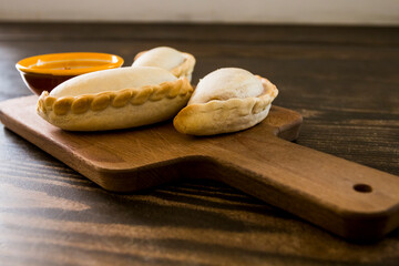 Traditional baked Argentine empanadas savory pastries with meat beef stuffing or vegetables against wooden background and spicy sauce. Latin American fried food