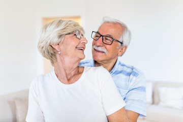 Elderly couple standing in the living room. Portrait of happy senior couple embracing each other in living room at home. Old couple looking each other with love and smilling.