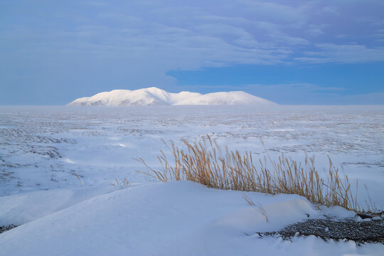 Winter Arctic landscape. View of the snow-covered tundra and mountains. Cold and windy winter weather. Harsh polar climate. Nature of Chukotka and Siberia. Anadyr tundra, Chukotka, Far East of Russia.