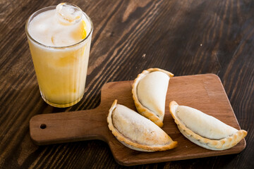 Traditional baked Argentine empanadas savory pastries with meat beef stuffing and vegetables against wooden background with spicy sauce and ice lemon tea, fresh and homemade. Latin food and drink