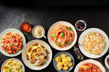 Italian food. Many different pastas, grated Parmesan cheese, ravioli, olives and wine, shot from above on a black background with a place for text