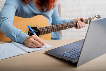A woman with a guitar writes notes in a notebook. The girl composes a song
