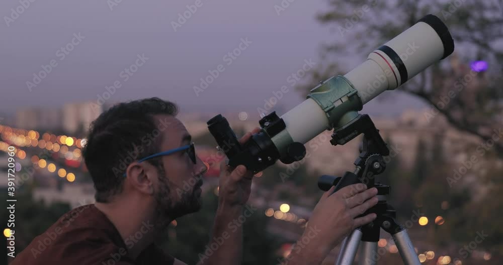Wall mural amateur astronomer looking at the stars with a telescope with blurred city lights in the background.