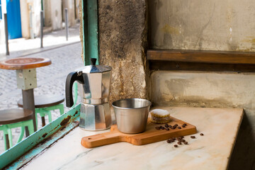 Italian lack coffee in a cup with coffee beans and a handmade cookie with sugar and a moka pot behind. Everything in vintage brown background close to the window.