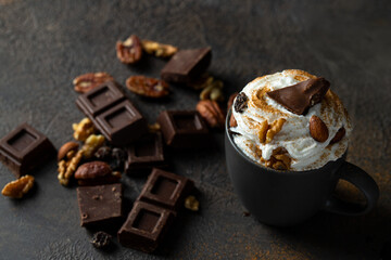 Hot chocolate in mug decorated with whipped cream, chocolate slices and nuts on concrete background. Traditional beverage for cold days concept.