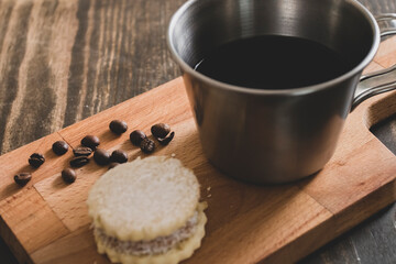 Italian american black coffee in a vintage cup with coffee beans around and a handmade cookie with sugar and a moka pot behind. Everything in vintage wood background 