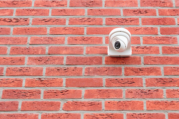 Low angle view on white cctv security camera mounted on a red brick wall. Security concept, big brother is watching