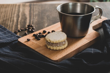 Italian american black coffee in a vintage cup with coffee beans around and a handmade cookie with sugar and a moka pot behind. Everything in vintage wood background 