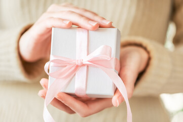 Girl holds in her hands a festive white box with a pink ribbon. A cozy surprise gift for a winter seasonal holiday. Festive lifestyle, hygge. Surprise packaging with decor