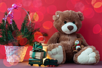 Christmas card with Teddy bear, gift box on toy locomotive, decorated christmas tree on red bokeh background.