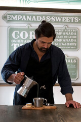 Male Barista preparing fresh espresso in coffee maker for customer in a fancy coffee shop. Cafe owner serving a client at the coffee shop