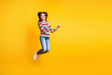 Fototapeta na wymiar Full length body size photo of jumping high schoolgirl pointing up at empty space isolated on vibrant yellow color background