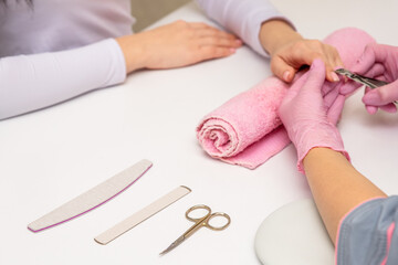 Close-up shot of a manicurist using a cuticle clipper to give a nail manicure to her client in the beauty salon. Master of manicure remove a cuticle nail with nail clipper.