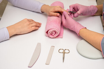 Close-up shot of a manicurist using a cuticle clipper to give a nail manicure to her client in the beauty salon. Master of manicure remove a cuticle nail with nail clipper.