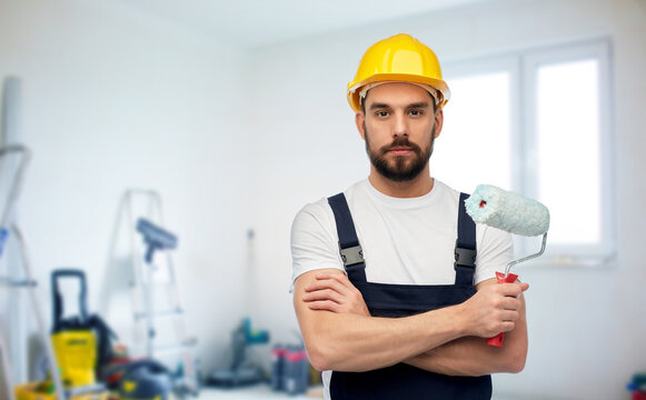 repair, construction and building concept - male worker or builder in yellow helmet and overall with paint roller over room with equipment on background