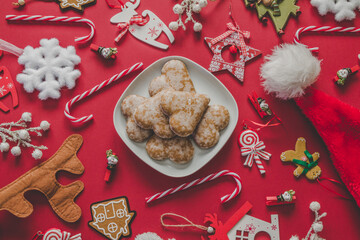 Christmas table flat lay composition. Delicious heart-shaped gingerbread cookies, candy canes, Santa hat and Christmas Tree ornaments and decorations.