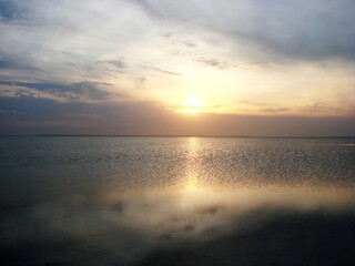 The landscape of the evening sun hides behind the clouds on the horizon, and is reflected by a sunny path on the calm surface of the shallow lake Sivash.