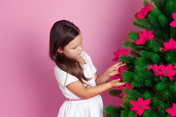 profile portrait of a beautiful girl in a white dress decorating a Christmas tree with mistletoe...