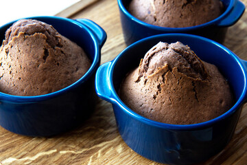 Delicious baked chocolate muffins in violet ceramic tins on wooden background. Side view. Close up