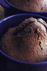 Delicious baked chocolate muffins in violet ceramic tins on wooden background. Side view. Close up