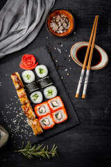 Japanese rolls, soy sauce and sticks on black slate board and black background top view, vertical photo