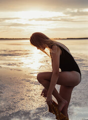 Fototapeta na wymiar Beautiful young blonde with long hair dresses up on the lake shore. Walk during sunset. Girl in a bathing suit