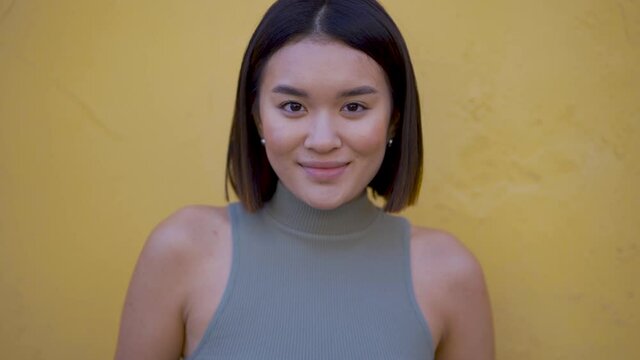 Portrait of young pretty asian female looking at camera and smiling outdoors. Front view.