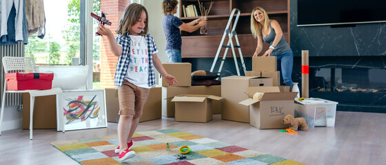 Little boy playing with a toy airplane while his parents unpack moving boxes