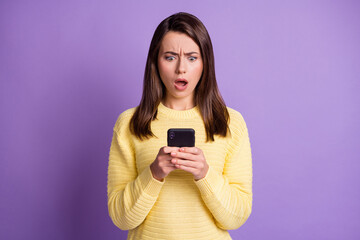 Photo portrait of upset nervous girl holding phone in two hands with open mouth isolated on vivid violet colored background