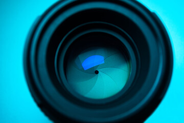 Close up camera lens reflection  under light blue neon light with colorful neon highlights against light blue background