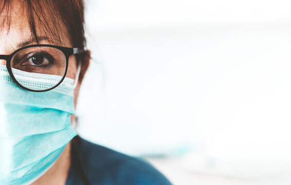 Close up portrait of a serious female nurse with protective mask and medical uniform - white copy space on the right.
