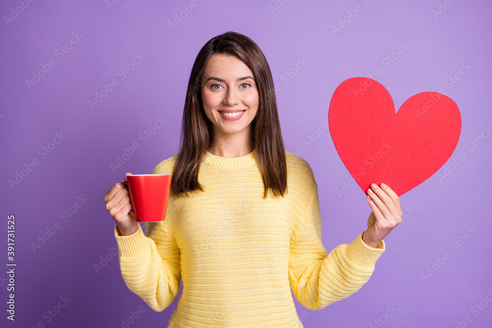 Poster Photo portrait of woman holding big red heart cutout in one hand with mug of cocoa smiling isolated on vivid purple colored background