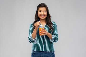 takeaway drinks and people concept - happy smiling young asian woman drinking orange juice from plastic cup with paper straw over grey background