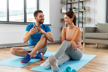 Obraz premium fitness, sport and technology concept - happy young man showing with smartphone to woman at home