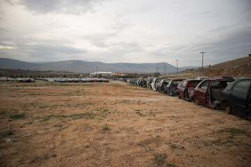 Half cut cars in a line, before the dusk. At a vehicle cemetery. Awaiting recycle or re-sale. More automobiles in background.