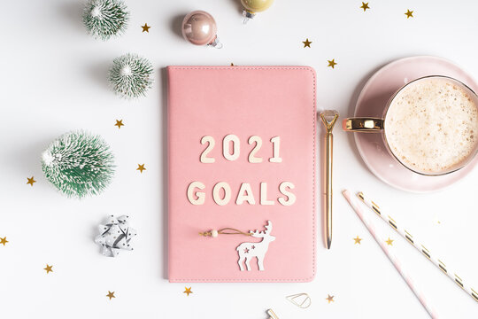Desktop Christmas notepad with 2021goals letters text. Flat lay of white table background with planner, cup of coffee, Christmas decoration and stationery.