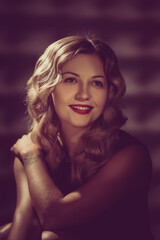 Fototapeta premium Beautiful young woman with curly blonde hair and bright makeup. image toned in warm colors in retro style