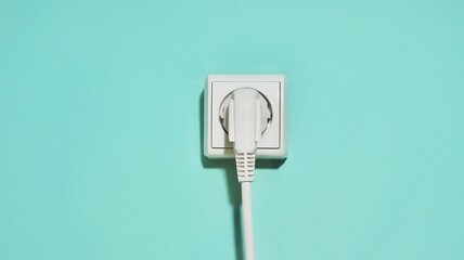 White electrical plug in white socket on turquise background. European white outlet in the center in green background . Copy space. Space for your text.