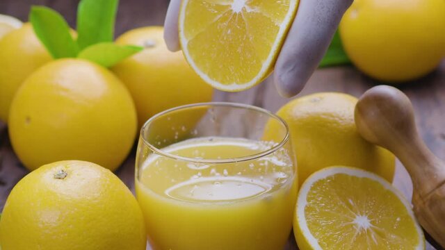 Half of an orange is squeezed into a glass of orange juice, surrounded by many ripe oranges with leaves.