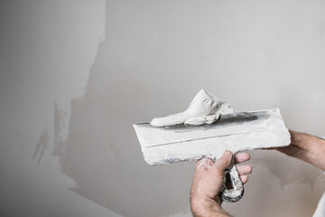 A construction worker puts white putty on a spatula from a bucket. Close-up