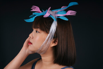 Young asian thai black short hair with utensil fork and spoon headband over dark background.
