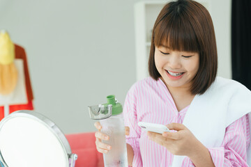Young asian thai short hair bob hairstyle drinking water from bottle and using smartphone.
