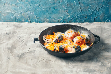 grated carrots and sliced fresh mackerel fish lie in a frying pan for preparing lunch
