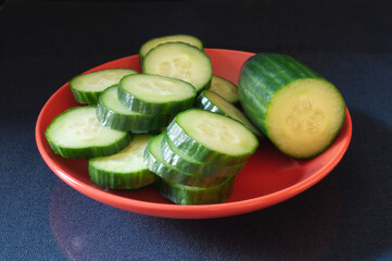 Green cucumber in red plate on black background