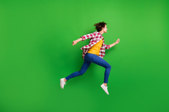 Full size profile photo of cute sweet girl jumping run hands fists wear trousers shirt sneakers isolated on green color background